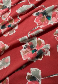 Material textil roșu cu modele florale abstracte mari, în nuanțe de roz, verde și marron. Materialul pare moale și ușor texturat.