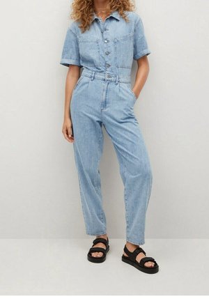 Combinaison en denim bleu clair à manches courtes, boutons à l'avant et deux poches poitrine. Caractérisée par une taille haute et un pantalon à coupe décontractée. Sandales noires.