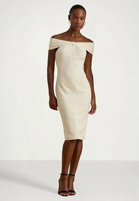 Sømløs off-shoulder kjole i kremfarget stoff med ribbestruktur, kne-lang, med en midt-bue detalj. Inkluderer stiletthæler.