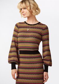 Maglione a maglia con motivo ondulato multicolore nei toni del verde, rosa e oro. Presenta maniche lunghe a sbuffo e un orlo in vita e polsini neri aderenti.