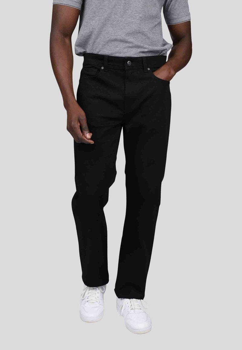 Jean en denim noir avec une coupe droite, cinq poches et passants de ceinture, associés à un polo gris et des baskets blanches.