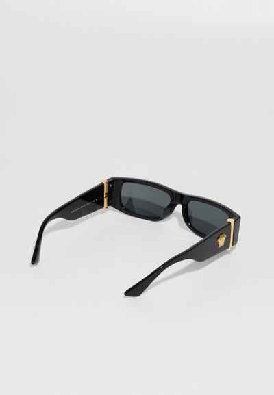 Black sunglasses with a rectangular frame, dark lenses, gold hardware accents, including a lion logo on the temple, and glossy finish.