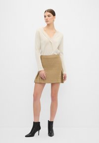 Beige långärmad topp med V-ringning; guld texturerad minikjol med sidslitsar; svarta ankelskor. Enkel, skräddarsydd design.