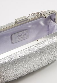 Pochette argentée ornée de strass brillants, fermoir à cadre métallique et intérieur en satin violet clair, étiquetée "L.CREDI Munich."