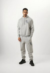 Gray hoodie and sweatpants set made of soft fabric. Features a front pocket, drawstring hood, and logo accents on both pieces.