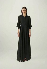 Svart långärmad klänning av flödande tyg, med knapp fram, cinchad midja med band och voluminösa puffärmar.