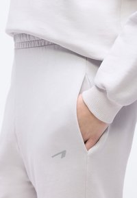 Χέρι στην τσέπη ανοιχτόγκρι ελαστικού στη μέση παντελονιού φόρμας, φορεμένο με μανίκι φούτερ με ριμπ μανσέτα που ταιριάζει.