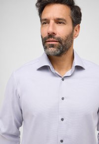 Hellblaues Button-Up-Hemd aus strukturiertem Stoff mit kontrastierendem gemustertem Innenkragen. Verfügt über schwarze Knöpfe und lange Ärmel.