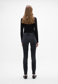 Fekete, slim-fit farmernadrág, közepes derékszámmal, hátsó zsebekkel és minimalista dizájnnal. Fekete, testhezálló toppal viselve.
