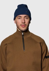 Granatowa dzianinowa czapka i brązowy polar na zamek z wysokim kołnierzem. Polar ma pionową fakturę i czarny zamek błyskawiczny. Prosty design.