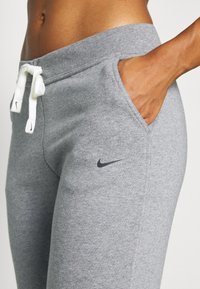 Graue Nike_Sweatpants mit weicher Textur, elastischem Bund, weißem Kordelzug und Seitentaschen. Enthält ein kleines schwarzes Logo auf dem Oberschenkel.