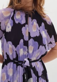 Pleatattu mekko mustalla taustalla, jossa on kukkakuosi purppuran ja kermaisen sävyissä, lyhyet hihat ja vyötäröllä solmittava vyö.