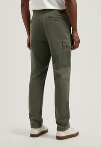 Groene cargo broek met zijzakken, rechte benen en een subtiele textuur. Gekleed met witte sneakers en een lichtgekleurde shirt.