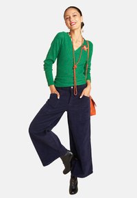 Green knit sweater with a v-neck, paired with navy wide-leg corduroy pants and black lace-up boots. Accessories include a red bag and a necklace.