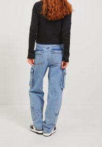 Pantaloni cargo in denim azzurro chiaro con tasche laterali, vestibilità comoda e un finish leggermente sbiadito. Indossati con un maglione aderente nero e sneakers.