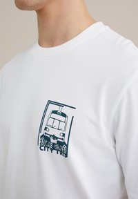 Balta medvilnės marškinėliai su mėlynu traukinio piešiniu stačiakampio kontūre, po dizainu esantis tekstas "CITY TRIP".
