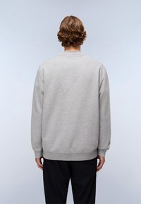 Grijze trui van zacht stof, met een ronde hals en geribbelde manchetten. De achterkant is effen met een losse pasvorm, gecombineerd met donkere broek.