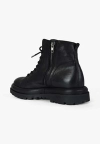 Stivaletti alla caviglia in pelle nera con punta arrotondata, suola in gomma spessa, cerniera laterale e chiusura frontale con lacci. Finitura testurizzata con accenti opachi.