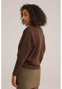 Bruine oversized trui met een zachte textuur, geribde manchetten en zoom. Draagt bij een strakke, olijfgroene rok, wat een relaxed silhouet laat zien.