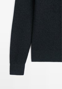 Dark blue knitted sweater sleeve featuring a textured pattern and ribbed cuffs, made of a soft, medium-weight material.