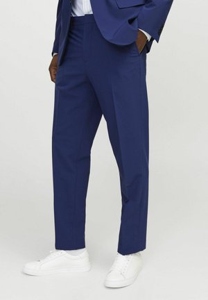 Marineblaue Anzughose aus leichtem Material mit geradem Bein. Verfügt über seitliche Taschen und eine glatte Textur. Getragen mit weißen Sneakers.