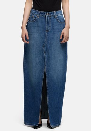 Person trägt einen hoch taillierten, dunkelblauen Jeans-Maxi-Rock mit einem vorderen Schlitz, schwarze spitze Schuhe und ein schwarzes Oberteil.