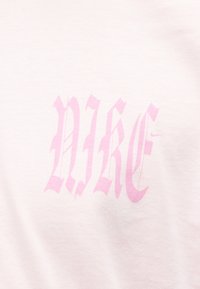 Ροζ γοτθικό κείμενο "NIKE" τυπωμένο σε ανοιχτό ροζ ύφασμα.