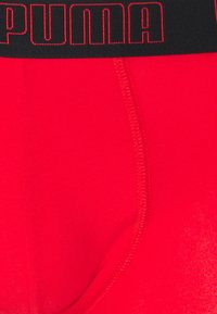 Rote Baumwoll-Boxershorts mit einem schwarzen elastischen Bund, der das kontrastierende rote "PUMA"-Logo zeigt. Glatte Textur mit sichtbaren Nähdetails.
