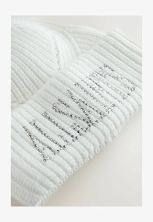 Balta adīta cepure ar ribotu tekstūru, kuras iešūtajā malā ir izšūts vārds "ziema" ar sudraba pērļu rotājumu.