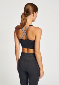 Svart sport-bh med grå remmar och ribbad textur; ihopkopplad med höga svarta leggings som har vertikala linjer och geometriska utskärningar.