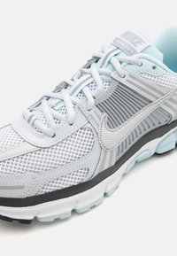 Light gray mesh running shoe with silver accents and light blue highlights. Features a padded collar, lacing system, and textured sole.