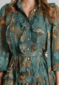 Vestido verde agua con bordado floral en dorado y óxido, que presenta detalles con volantes, cierre de botones y un cinturón de tela a juego.