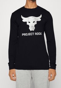 Chemise noire à manches longues en coton avec un graphique de crâne de taureau blanc et le texte "PROJECT ROCK" imprimé en dessous.