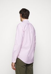 Långärmad skjorta i ljusrosa med vita vertikala ränder, med en bakstycke och knäppta manschetter. Tyget verkar slätt och stelt.