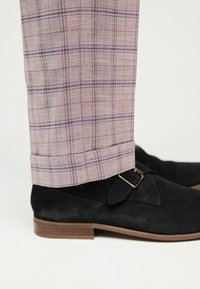 Schwarze Wildlederschuhe mit niedrigem Absatz, kombiniert mit hellrosa karierten Hosen, die lila Akzente und einen umgeschlagenen Saum haben.