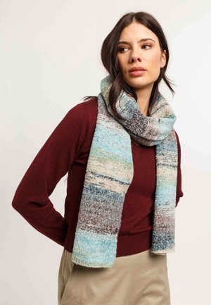 Écharpe multicolore avec un motif dégradé, présentant des textures douces dans des nuances de bleu, gris et beige, portée sur un pull bordeaux.