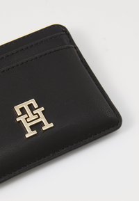 Crni kožni držač kartica s višestrukim utorima, s zlatnim logotipom i vidljivim detaljima šivanja, glatke teksture.