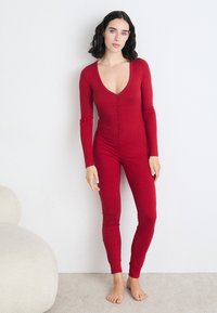 Piros, hosszú ujjú bodysuit mély V-kivágással és elől gombokkal. Bordás anyagból készült, testhezálló fazonnal és keskeny lábszárral rendelkezik.