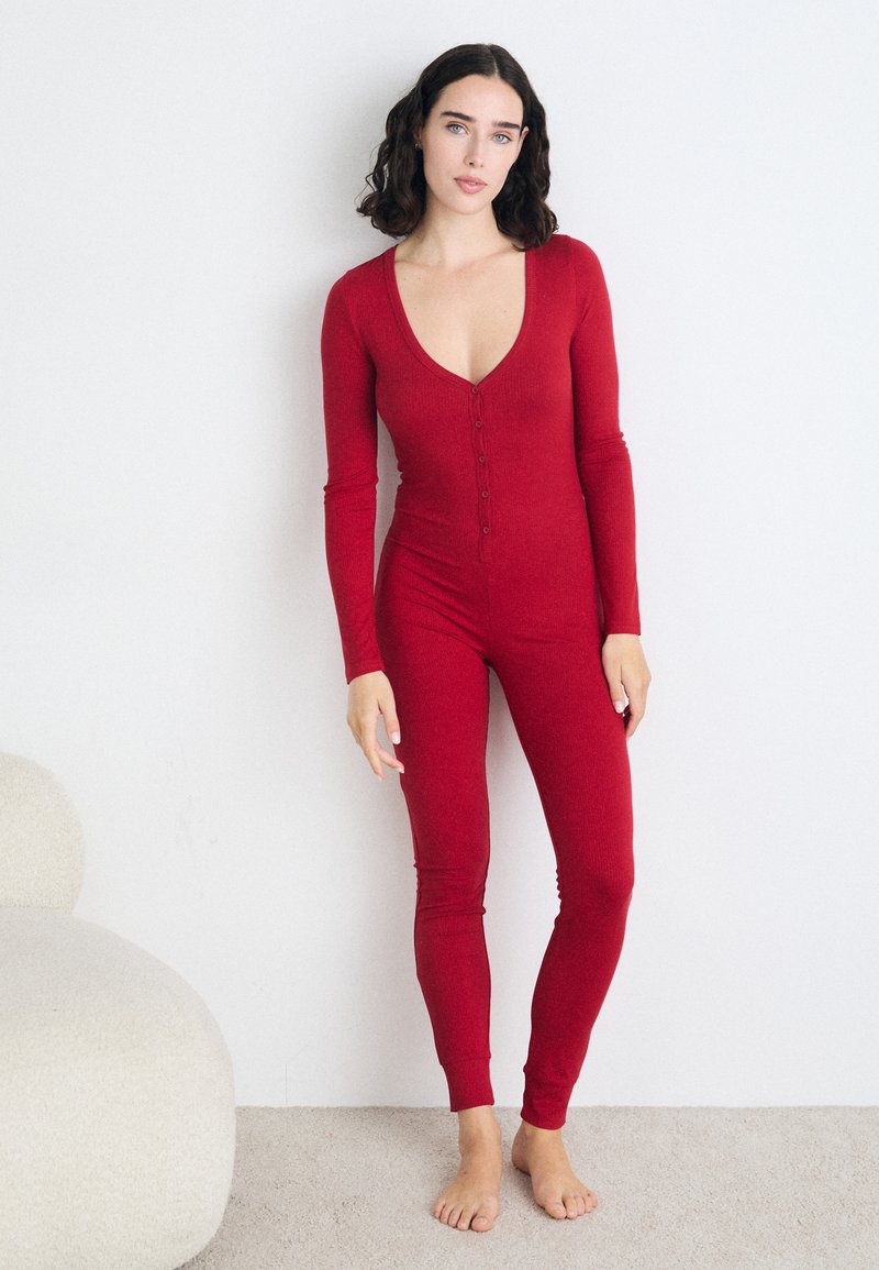Piros, hosszú ujjú bodysuit mély V-kivágással és elől gombokkal. Bordás anyagból készült, testhezálló fazonnal és keskeny lábszárral rendelkezik.