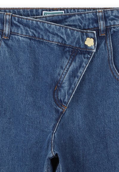 Ciemnoniebieskie dżinsy z unikalnym asymetrycznym krojem, złotym guzikiem w kształcie kwiatu oraz pomarańczowymi przeszyciami.