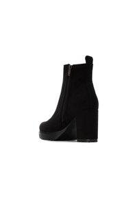 Botines de ante negros con una textura suave, un cierre lateral y un tacón alto y grueso. El diseño presenta una punta redondeada y acentos mínimos.