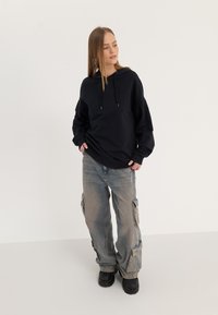 Black hooded sweatshirt with long sleeves, paired with light blue cargo pants featuring side pockets and a relaxed fit. Black boots complete the look.