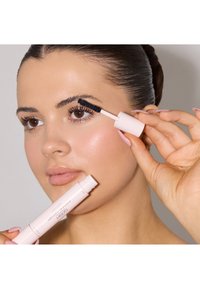 Ljust rosa mascara-förpackning hålls av en person, med en svart borste. Fokusera på väldefinierade, mörka ögonfransar och klar, slät hud.