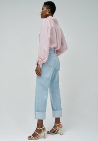 Blusa de manga larga rosa claro con puños atados, combinada con jeans de tiro alto azul claro con dobladillos enrollados y sandalias de tacón alto beige.