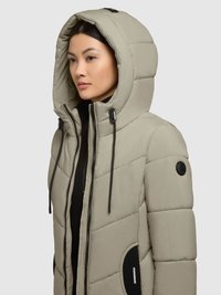Jachetă pufoasă de un bej deschis, cu glugă, având un design matlasat, accente negre, șnururi ajustabile și închidere cu fermoar.