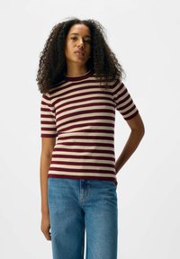 Top court à manches courtes en tricot rayé dans des tons bordeaux et beige. Doté d'un col rond et d'une silhouette ajustée, associé à un jean bleu taille haute.