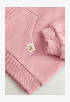 Roosa sviiter sileda tekstuuriga, ribidega varrukate ja äärtega, küljetaskuga ning sildi detailiga, millel on ringikujuline logo.