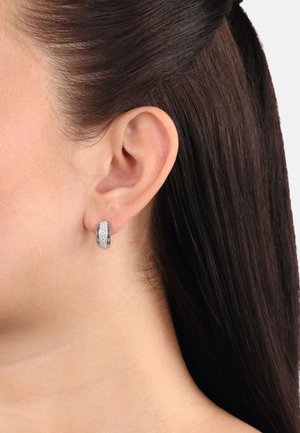 Orecchini a cerchio in argento con superficie texturizzata e dettagli scintillanti, progettati in forma arrotondata e indossati all'orecchio.