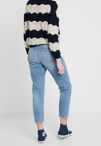 Hellblaue Jeans mit lockerer Passform und schmal zulaufenden Beinen, kombiniert mit einem navyblauen und cremefarben gestreiften Strickpullover und blauen High-Top-Sneakern.