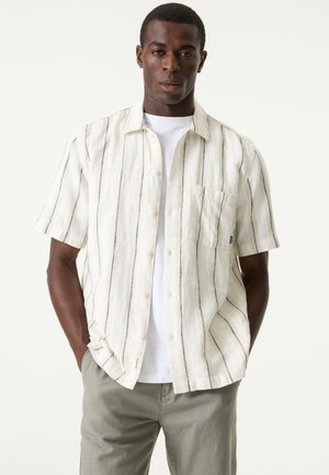 Kurzärmeliges, cremefarbenes Hemd mit vertikalen blauen Streifen, aufgesetzter Brusttasche und Button-Down-Kragen, getragen über einem weißen T-Shirt.